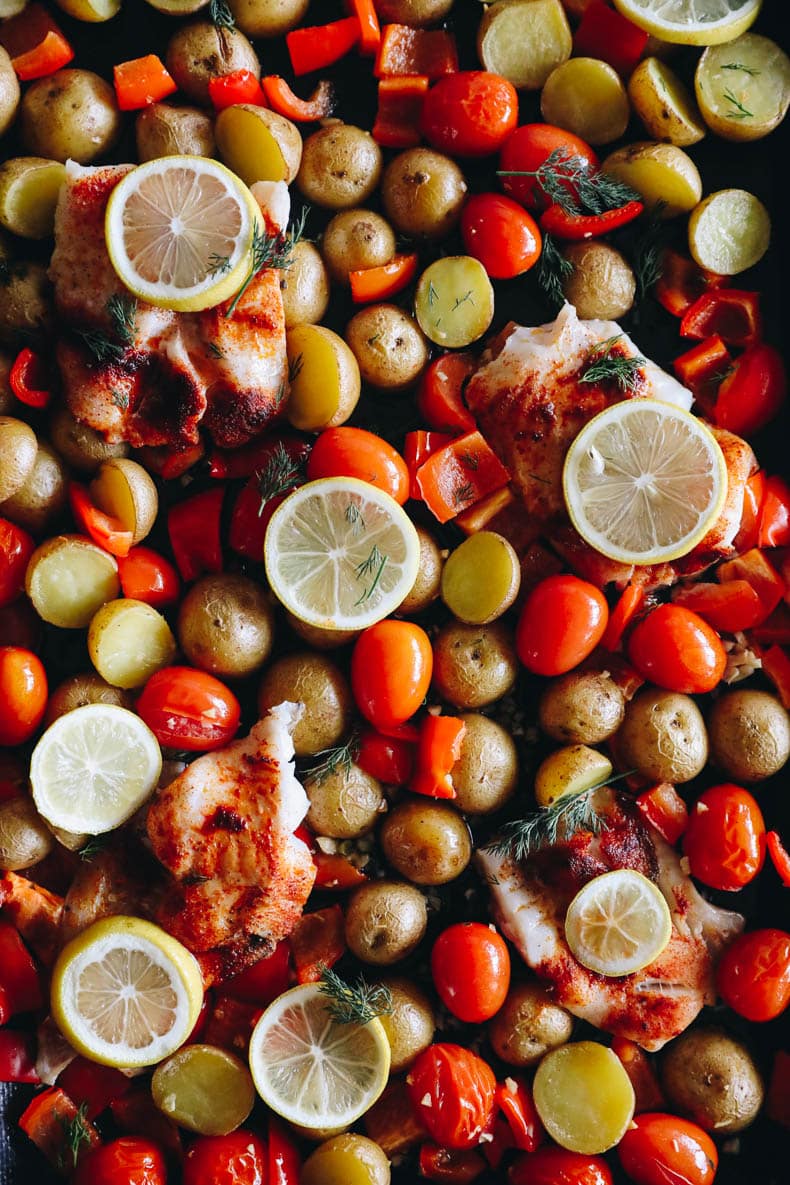 baked cod recipe on a sheet pan with roasted veggies, lemon slices + herbs