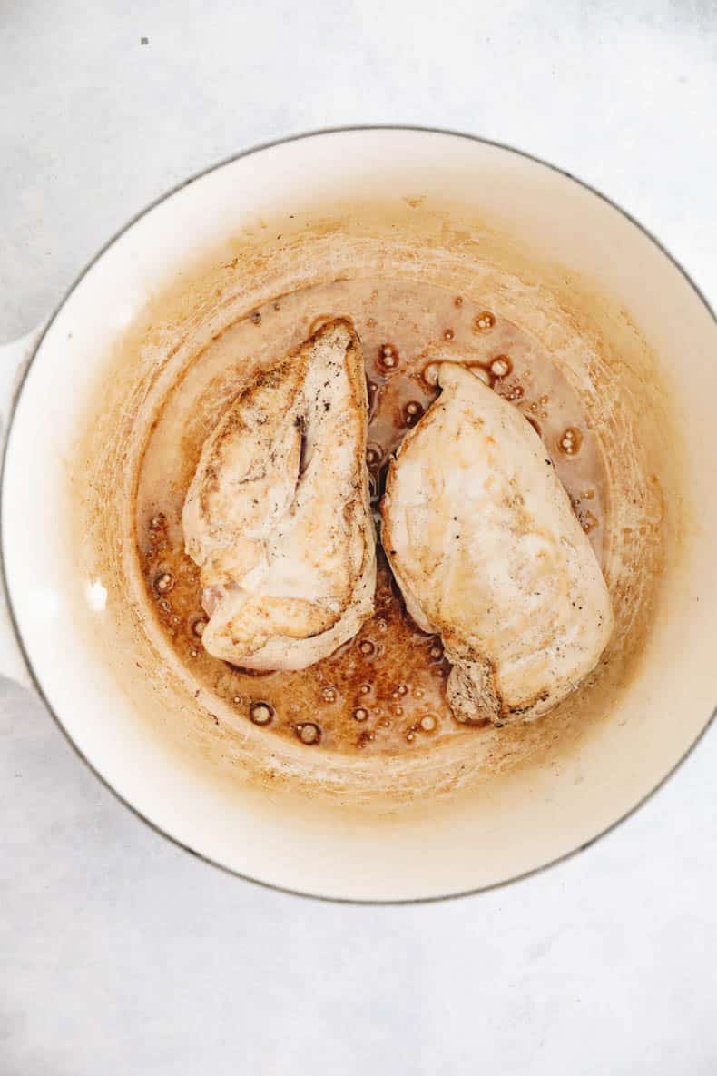 Chicken breasts cooked in butter in a white dutch oven.