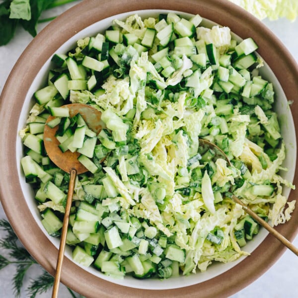 overhead image of a cabbage green goddess salad in a white and brown bowl with gold salad tongs.